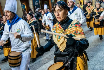Una mujer con mantón toca el barril mientras los cocineros pasan a su lado, en una calle de la Parte Vieja.