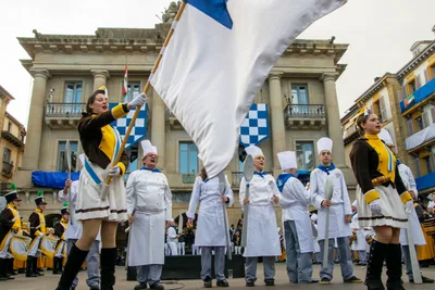 Una cantinera hace ondear la bandera delante del antiguo Ayuntamiento, con los cocineros alineados.