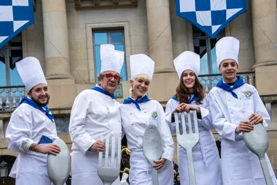 Cinco cocineros posan con los cubiertos gigantes delante de los balcones con banderas.