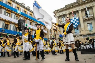 La cantinera ondea la bandera por encima de la formación, con la plaza llena detrás.
