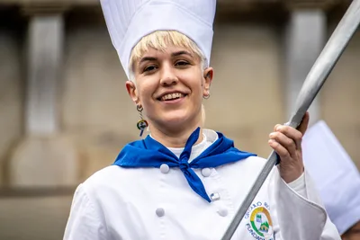 Una cocinera sonríe con la pala de cocina apoyada en el hombro.