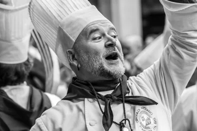 Retrato en blanco y negro de un cocinero cantando con el brazo levantado.