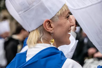 Una cocinera rubia de perfil, sonriendo bajo el gorro alto.