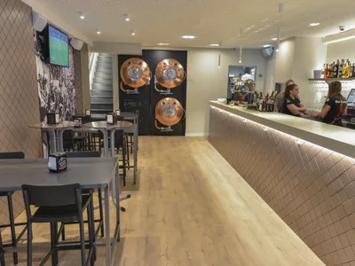 Campus Amara: barra alargada y, al fondo, tres tanques de cobre de cerveza en la pared.