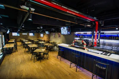 Sala del Campus de Gros: mesas de madera, pantallas en las paredes y una barra larga con los tubos rojos de la cerveza de bodega.