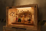 Otra caja de madera con «EXP:» pintado en la esquina, abierta como un pequeño escenario: una cueva encalada con cazos de cobre colgados de la pared, una bailaora de plastilina con vestido amarillo de lunares, un guitarrista y dos hombres sentados que la miran.